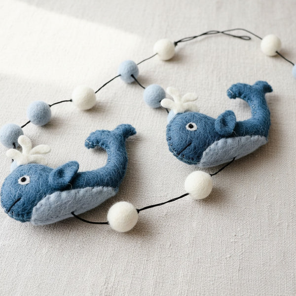Close up of the felt whale garland on linen, showing the needle felted wool texture and stitching