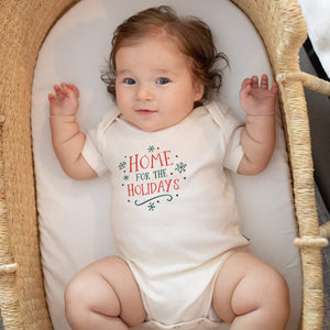 Graphic bodysuit for babies, "Home for the Holidays," short sleeve, angle view showcasing festive design.
