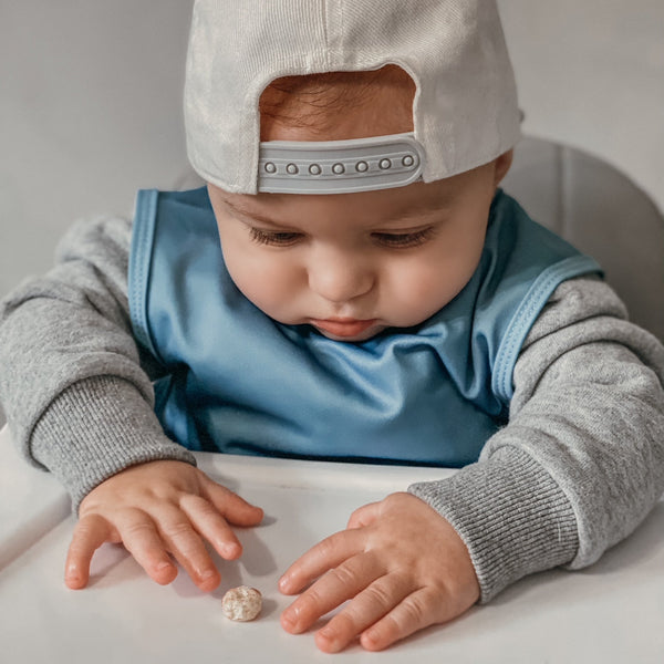 Solid dusty blue minimalist bapron for babies, angled view showcasing its stylish and functional design.