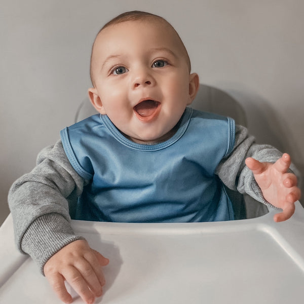 Solid dusty blue minimalist bapron for babies, angled view showcasing its stylish and functional design.