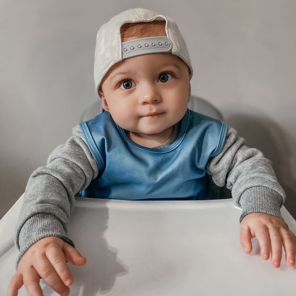 Solid dusty blue minimalist bapron for babies, angled view showcasing its stylish and functional design.