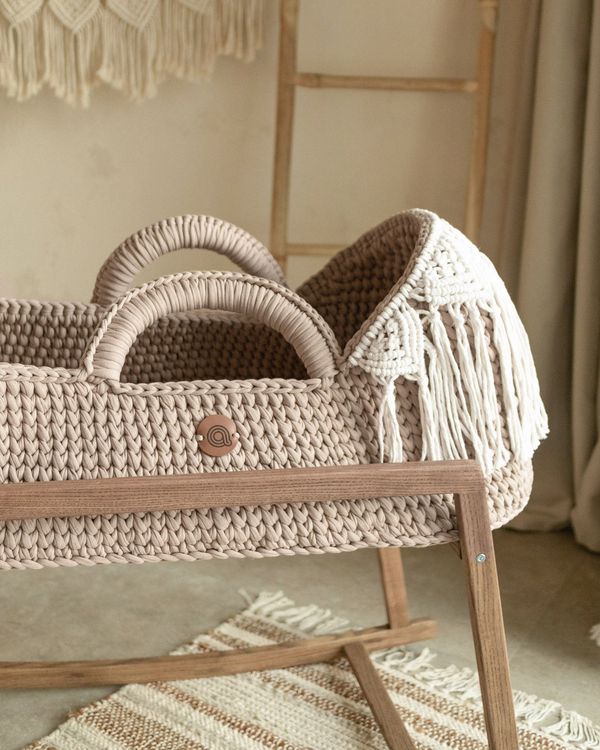 Knitted boho Moses basket with macrame hood on a wooden stand in a nursery