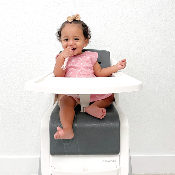 Blush Dino Friends Bapron for babies, angled view showcasing playful dinosaur design and practical bib features.