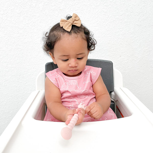 Blush Dino Friends Bapron for babies, angled view showcasing playful dinosaur design and practical bib features.