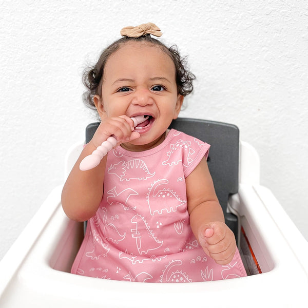 Blush Dino Friends Bapron for babies, angle view showcasing playful design and practical features.