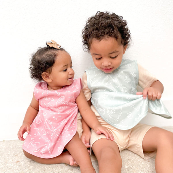 Blush Dino Friends Bapron for babies, angled view showcasing playful dinosaur design and practical bib features.