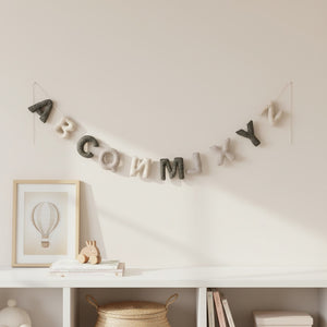 Felt alphabet garland draped along a white nursery shelf above a crib in soft daylight