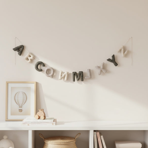 Felt alphabet garland draped along a white nursery shelf above a crib in soft daylight
