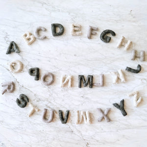 Neutral gray and cream felt alphabet letters arranged in a circle on a marble surface