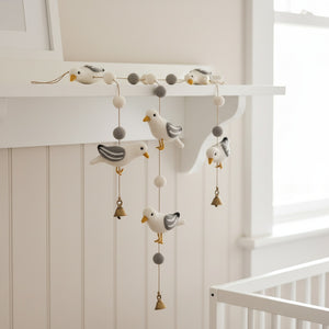 Felt seagull garland draped along a white nursery shelf, soft daylight on the wool birds