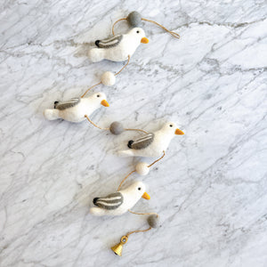 Felt seagull garland laid on marble, close view of the wool birds, pom poms, and hanging bell