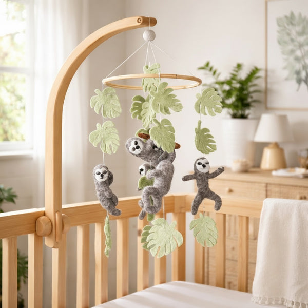 Wool felt sloth mobile hangs above a light wood crib in a calm, sunlit nursery