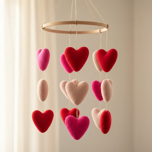 Felt heart ornaments in red and pink shown up close against a soft cream wall