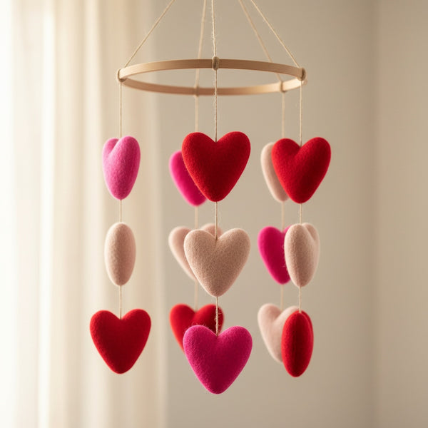 Felt heart ornaments in red and pink shown up close against a soft cream wall