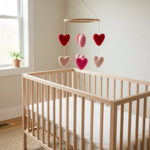 Felt heart ornaments hanging above a light wood crib in a bright, calm nursery
