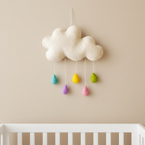 Handmade felt cloud wall hanging with five pastel raindrops on a beige nursery wall above a crib