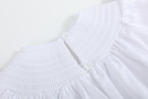 White and pink bows smocked bishop dress for babies, angle view showcasing its charming design and delicate details.