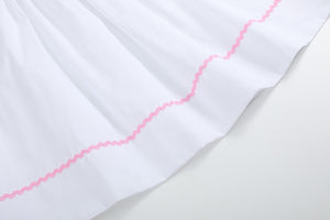 White and pink bows smocked bishop dress for babies, angle view showcasing delicate design and craftsmanship.