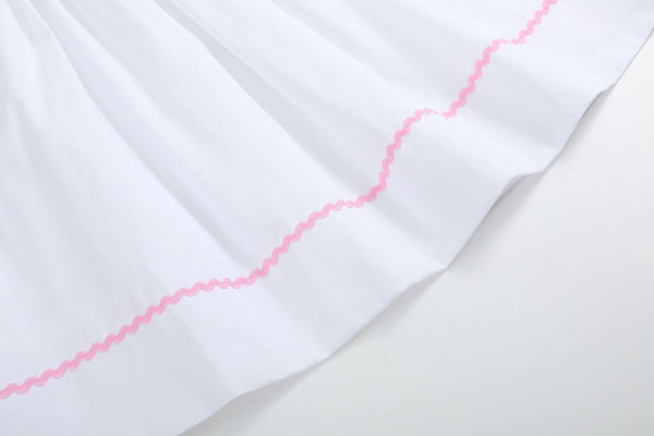 White and pink bows smocked bishop dress for babies, angle view showcasing delicate design and craftsmanship.